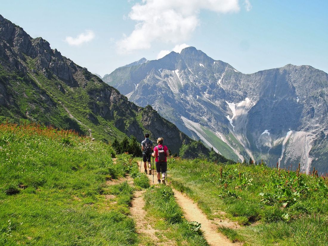 Two hikers walking a mountain trail toward a high peak